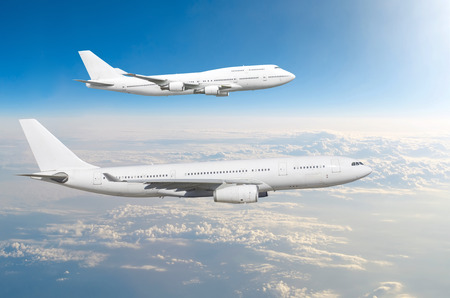 Two large white passenger airplanes fly parallel to each other in the sky above the cloudsの写真素材
