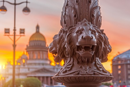 St. Isaac's Cathedral in the square, in St. Peterburg in the evening on a bright orange crane sunset sky, in the foreground the lions sculptureの写真素材