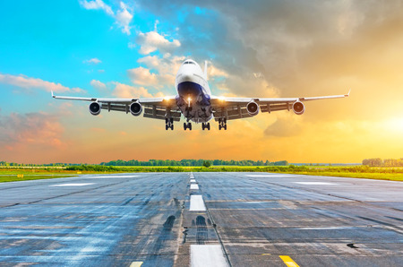 Aircraft with four engines flying arrival landing on a runway in the evening during a bright red gradient sunsetの写真素材