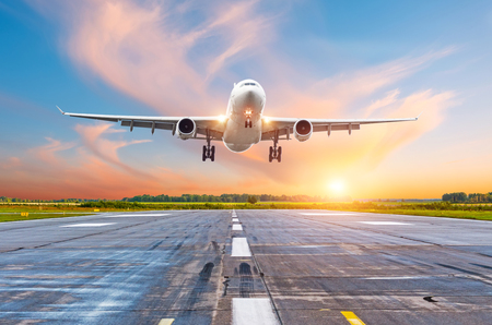 Airplane flying arrival landing on a runway in the evening during a bright red sunset sunshineの写真素材