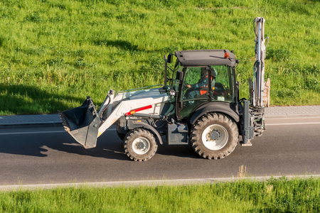 Tractor excavator with a bucket from the front behind, driving along the highwayの写真素材