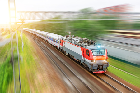 Electric locomotive with passenger cars passing rail road through the city at speed motion sunny dayの写真素材
