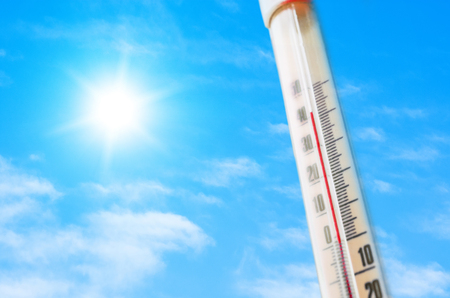 Thermometer against the background of an blue hot glow of clouds and sun, concept of hot weatherの写真素材