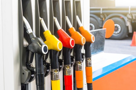 Pistols of gasoline fueling cars at the station, against the backdrop of a truck wheelの写真素材