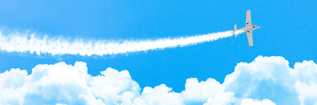 Light engine airplane with a trace of white smoke fly on cumulus clouds in summer, panoramaの写真素材