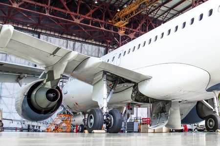 Passenger aircraft on maintenance of engine and fuselage repair in airport hangar. Rear view, under the wingの写真素材