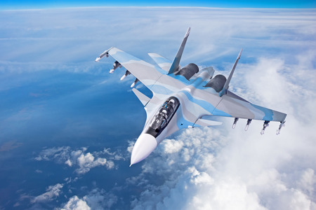 Combat fighter jet on a military mission with weapons - rockets, bombs, weapons on wings flies high in the sky above the cloudsの写真素材