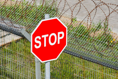 Red stop sign near the fence with barbed wireの写真素材