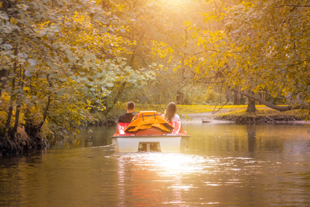 Couple in love in a catamaran, water bike in a park in autumn, sunsetの写真素材