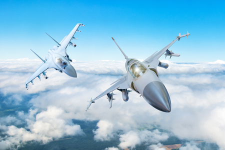 Pair of combat fighter jet on a military mission with weapons - rockets, bombs, weapons on wings flies high in the sky above the cloudsの写真素材
