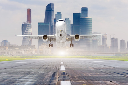 Commercial aircraft jetliner approaching for landing on runway, modern city on backgroundの写真素材
