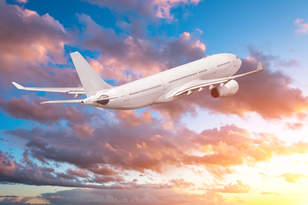 Airplane flying gaining height in the evening at sunset, the sky and picturesque cloudsの写真素材