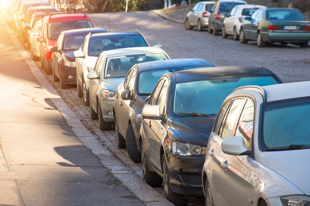 Many cars parked and lined up under trees on urban streetの写真素材