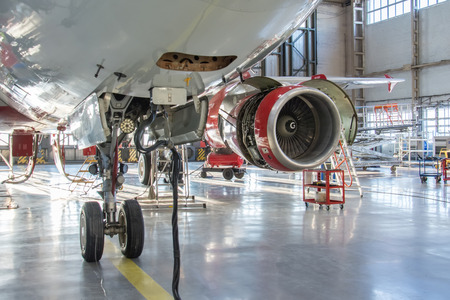 The front landing gear of an aircraft in service hangar in the background is an engine with an open hoodの写真素材