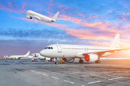 Parking at the airport with planes taking off and the sun in the evening skyの写真素材