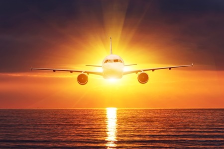 The plane flies in front of the sun. Sunset over the sea, view of the horizon. Water surface with waves.の写真素材