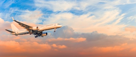 Passenger airplane is landing approach gear released, against sunset sky clouds, panorama. Travel...