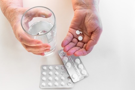 Hands of an elderly person with pills, packaging of medication. Glass of water. The concept of maintaining life in old age, treatment and healthの写真素材