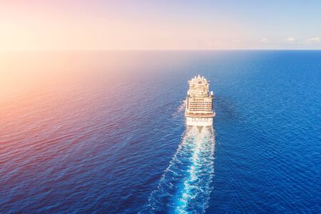 Cruise ship liner goes into horizon the blue sea leaving a plume on the surface of the water seascape during sunrise. Aerial view, concept of sea travel, cruisesの写真素材