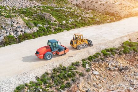 Roller and excavator on a dirt road before laying asphalt, aerial view