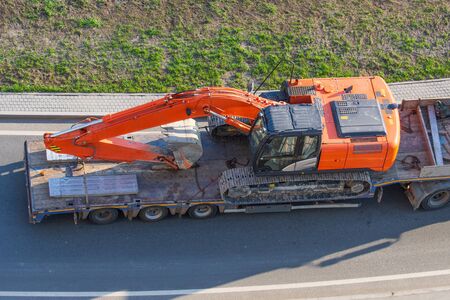 Truck with a long trailer platform for transporting heavy machinery, loaded excavator. Highway...