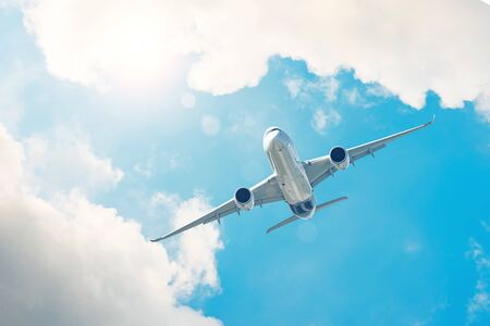 Passenger airplane gains altitude through the clouds in the background the bright sun shinesの写真素材