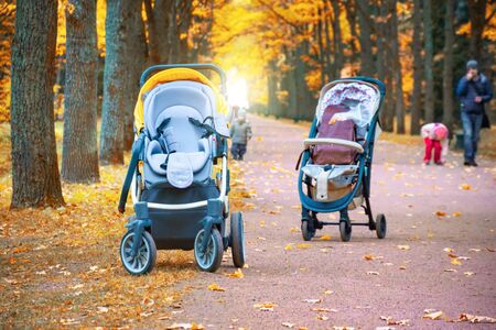 Two empty baby strollers for children stand on a path in the autumn parkの写真素材