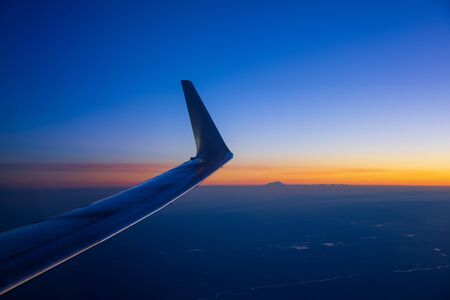 View of the wing of an airplane before dawn. Mountains and a peak are visible in the distanceの写真素材