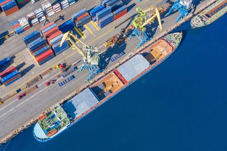 Aerial top view huge cargo ship moored at the pier at the port, loading goods, metal, concrete and...