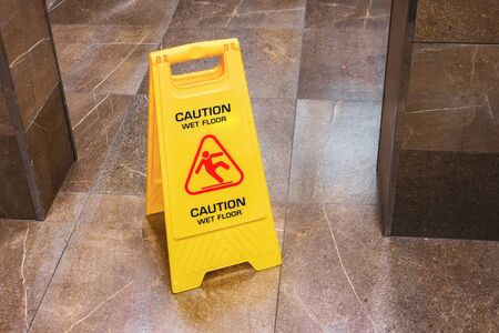 Yellow sign caution wet floor with a falling man in the hallway of the public toiletの写真素材