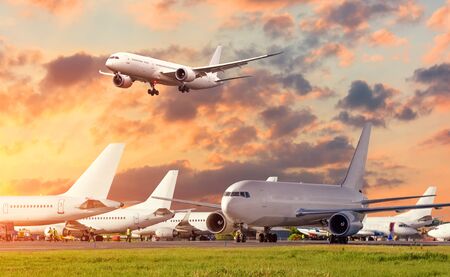 View of the standing aircrafts at the airport and airplane approach to landing in the skyの写真素材