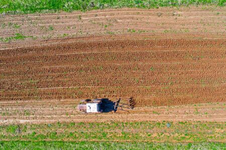 Tractor plows a small field in the village before planting vegetables. Aerial height view