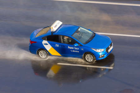 Blue passenger car Yandex Taxi rides on the wet rain spray highway aerial view. Russia, Saint-Petersburg. 15 may 2020のeditorial素材