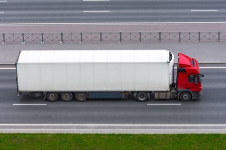 Truck with a white container on a trailer rides on a city highway, aerial side viewの写真素材