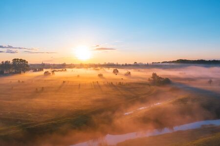 Morning fog in the meadows and at the mouth of the river during sunrise in the countryside, aerial...