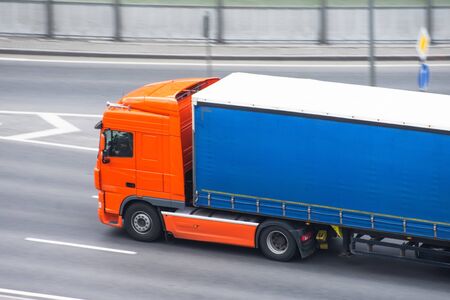 Yellow truck with a container on a trailer rides on a city highway, side aerial viewの写真素材