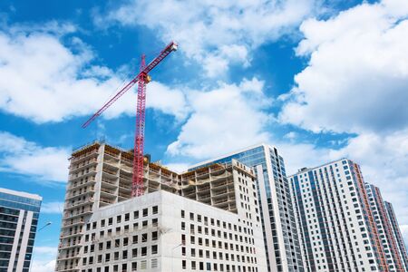 View of a multistorey building under construction with high construction cranes and a glass tower in...