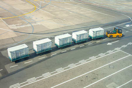 Empty luggage trolleys at the airport, for unloading bags of passenger airplane, amid tails of...