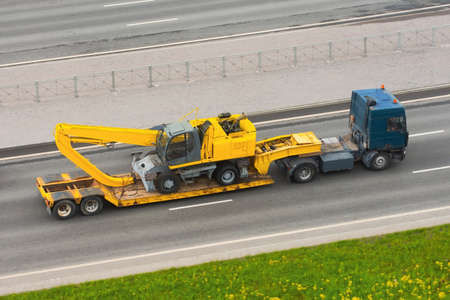 Heavy new yellow excavator long boom bucket on transportation truck with rubber wheels long trailer...