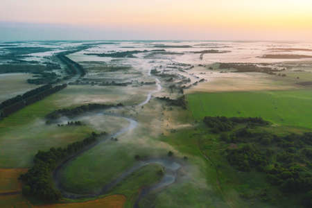 Evening foggy landscape in a valley of a small river among meadows and forests
