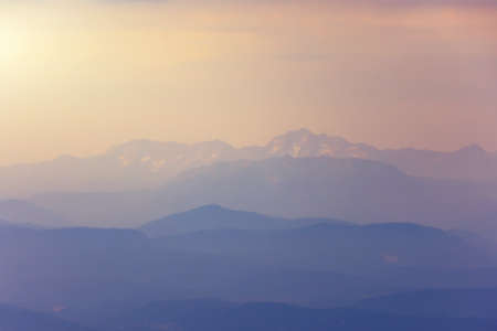 Silhouettes of snow mountains by the sea in the evening light with haze in the atmosphereの写真素材