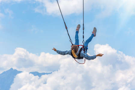 Girl swinging on a hanging swing over an abyss against the backdrop of mountains and sky and clouds