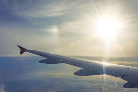 Wing view of the airplane on a winglets, fluffy clouds on the skyline sun rays haloの写真素材