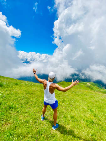 The guy on the top of the mountain ridge among the meadows looks in surprise at the sky with his...