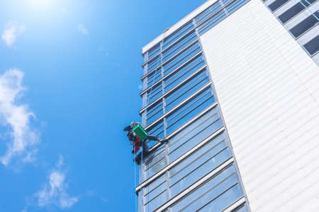 Climber clean windows from the outside of the building washing the glazing of the facade of a multi-storey buildingの写真素材