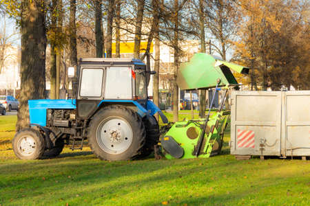 Vacuum sweeper towed by a tractor dumps into a container for harvesting leaves from city streets work in autumn parkの写真素材