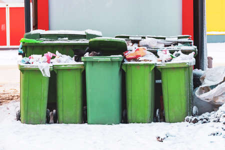 Overflowing trash cans with household waste on a snowy ice street