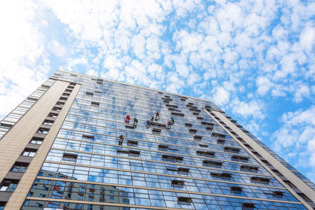 Climbers clean windows from the outside of the building washing the glazing of the facade of a multi-storey buildingの写真素材