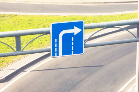 Blue road sign with an arrow turning from the outer lane on the background of a highway exitの写真素材