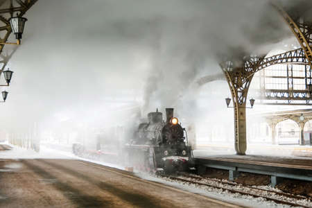Steam locomotive stands on the platform of the station, winter cold snowy day